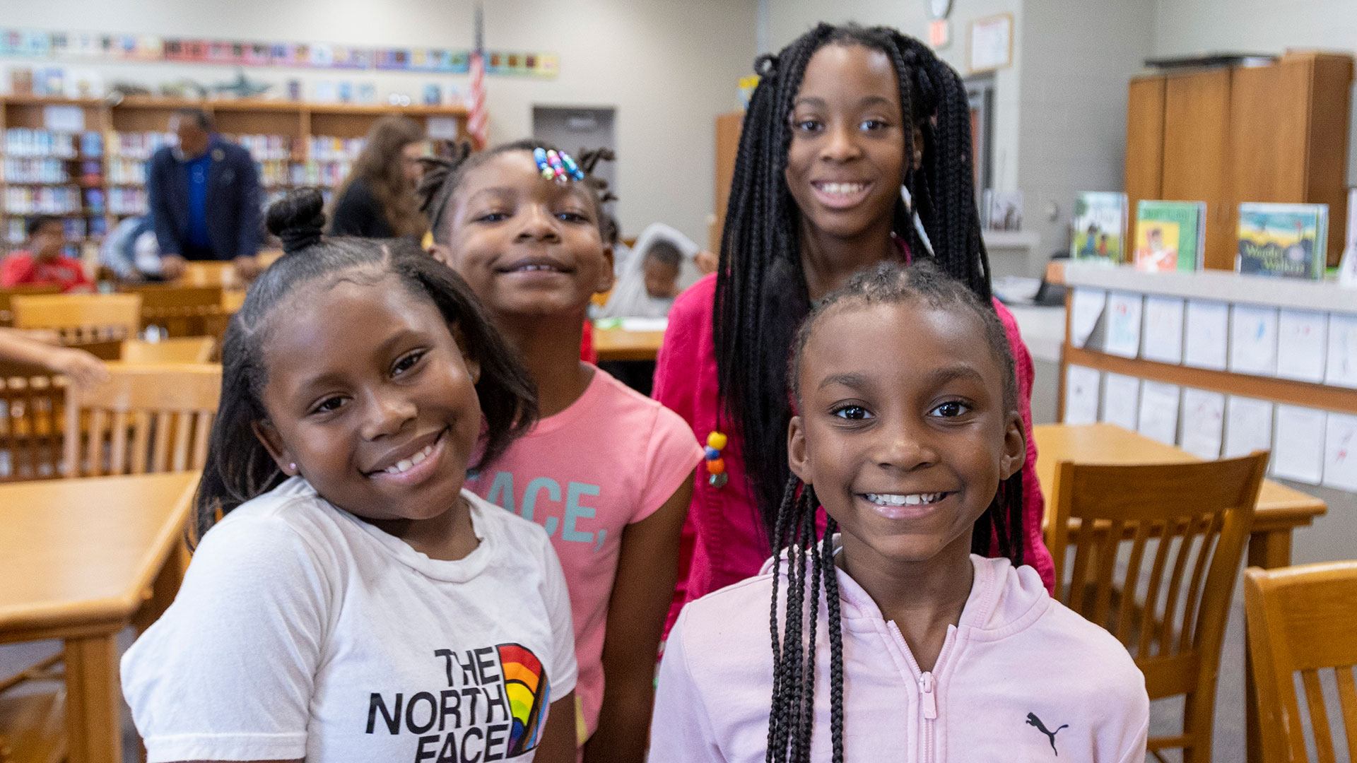 Four young girls in a library smliing.
