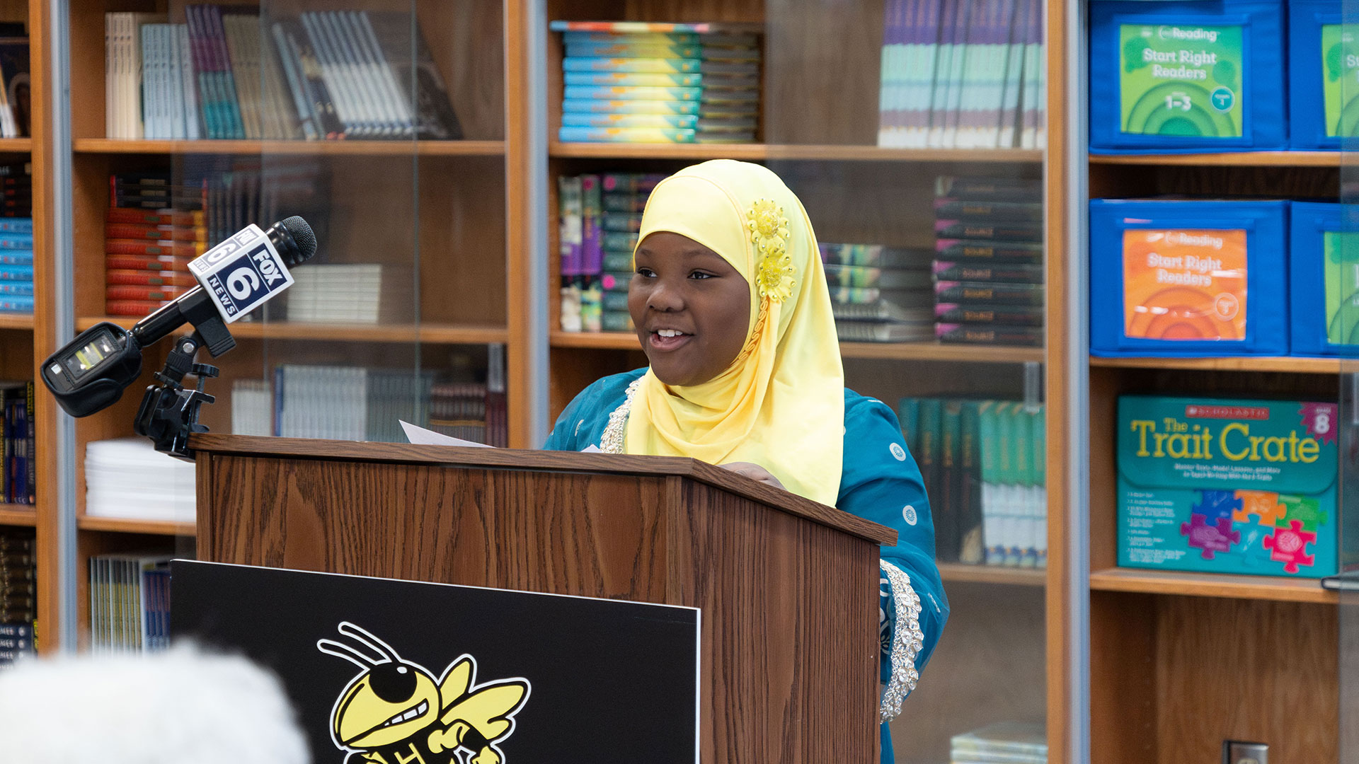 A young girl speaking at a podium in a library.