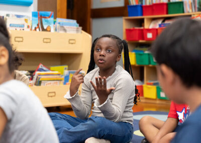 A young girl in a classroom using her fingers to count.