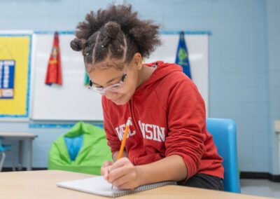 فتاة جالسة إلى طاولة تكتب في دفتر ملاحظات.