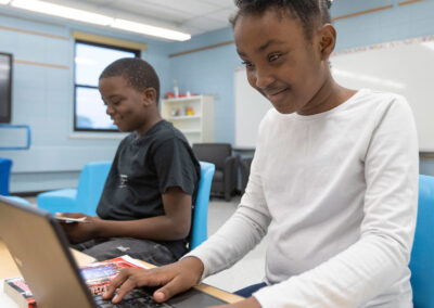 يجلس طالبان على طاولة، أحدهما يقرأ كتابًا والآخر يكتب على جهاز كمبيوتر محمول.