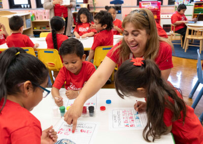 Una profesora ayuda a sus jóvenes alumnos a practicar el trazado del alfabeto.