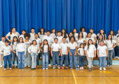 Un grupo de niños con vaqueros y camisas blancas posan en un auditorio.
