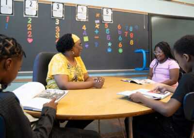 Three students sit at a table with their teacher and read.