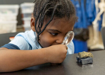 A little girl uses a magnifying glass to look at a rock.