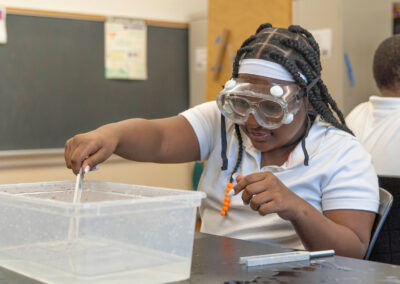 A girl wears googles as she puts a tuning fork into a bucket of water.