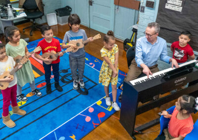 Overhead view of young students playing guitars as a teacher plays piano.