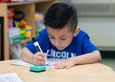 A young boy writes his name with a dry erase marker.