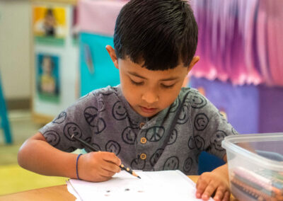 Un niño se sienta en una mesa y utiliza un lápiz de color.