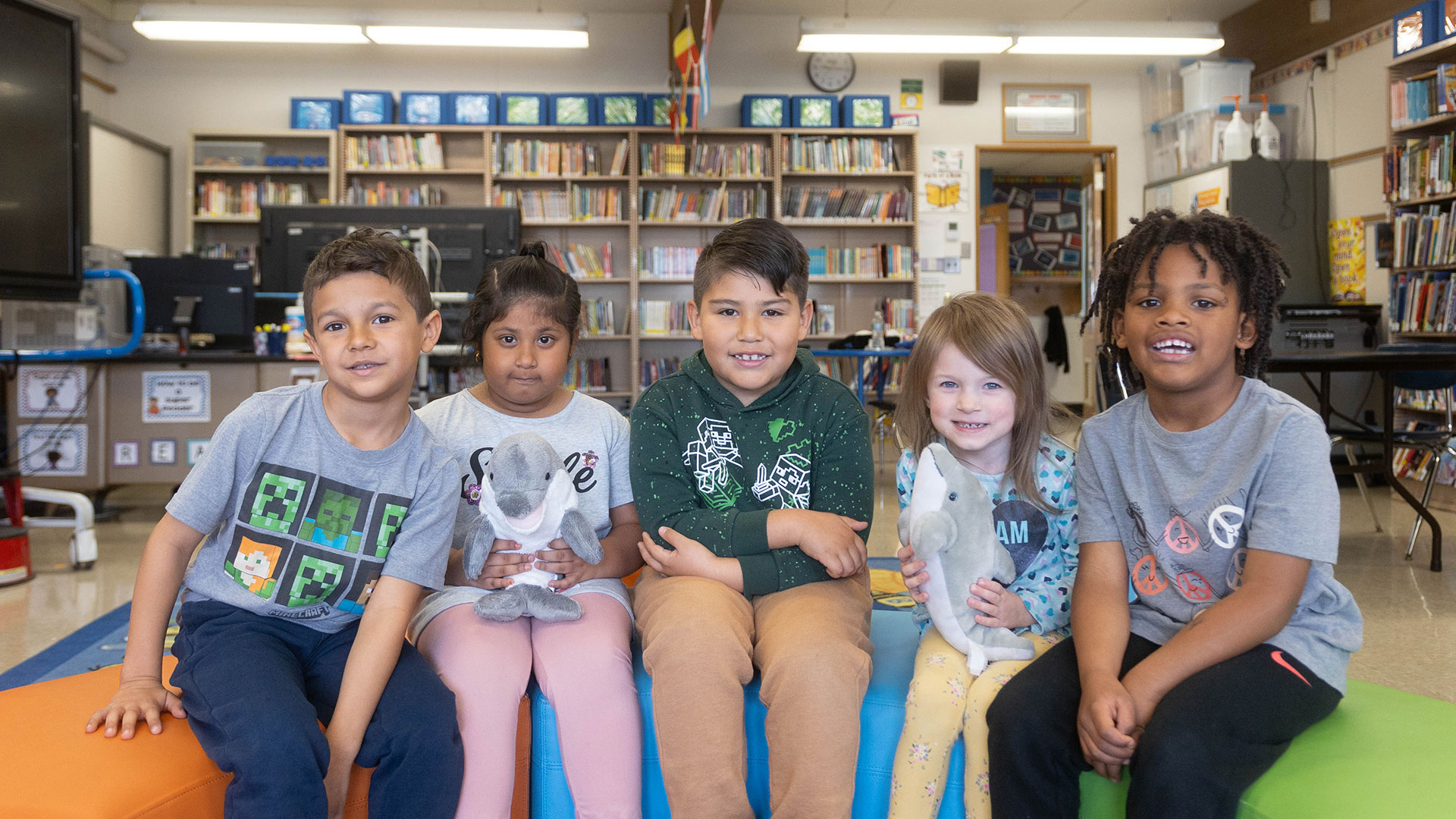 A group of young students in a library sitting on colorful furniture.