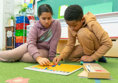 Two students sit on a rug and work together sorting colors.