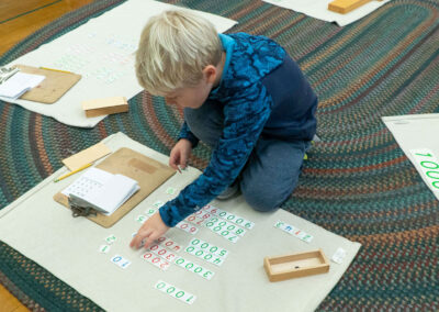 A boy sits on a rug and sorts numbers.