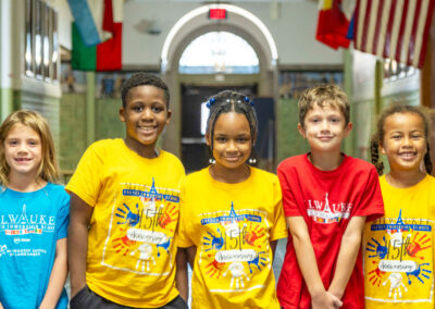 Five students in a hallway standing side by side in colorful Milwaukee French Immersion School shirts.