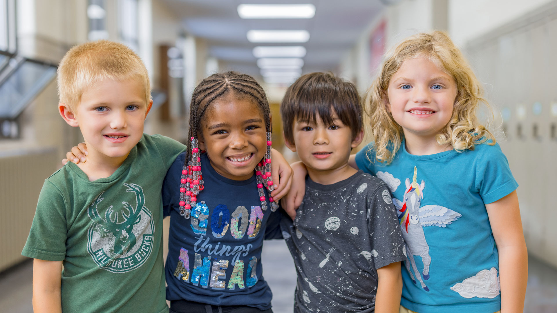 Four young children with their arms around one another in a school hallway.