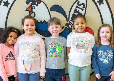 Five young children stand in front of a mural smiling.