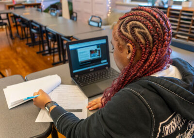 Over the shoulder view of a person referencing a computer to write and assignment.