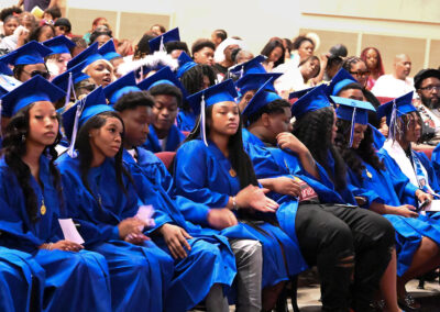 Graduates in caps and gowns sit in an auditorium.