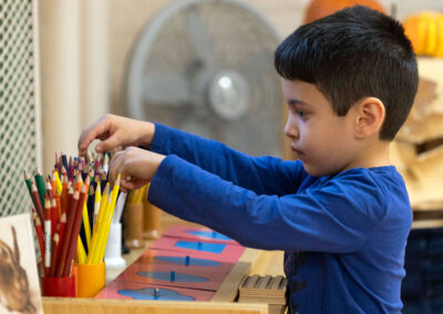 A young boy choosing a colored pencil from a cup.