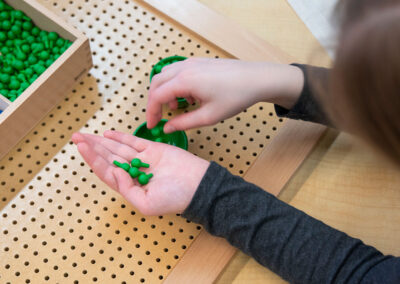 Overhead view of a child's hand holding green pegs over a pegboard.