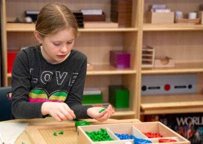 A girl sits at a table and sorts different color pegs.