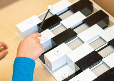 Close up of a young child's hand holding a mallet and playing a xylophone-like instrument.