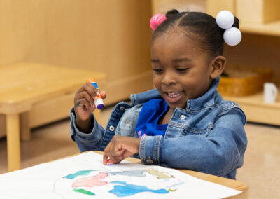 A young girl smiles with a glue stick in her hand.