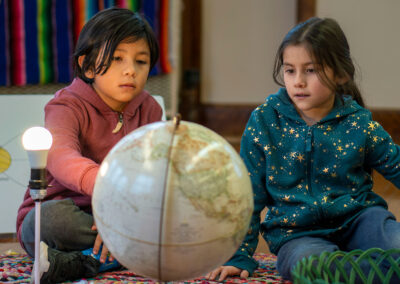 Two young students sit on the floor and look at a globe.