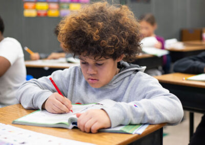 A boy in a classroom writing in a workbook.