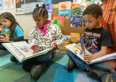 Children sit on a colorful rug as they look at picture books.