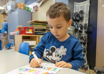 A boy at a table coloring letters.