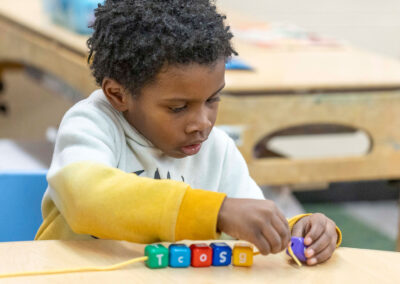 A young boy concentrates as he threads a cord through blocks.