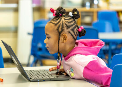 A young girl leans forward in her chair as she uses a laptop.