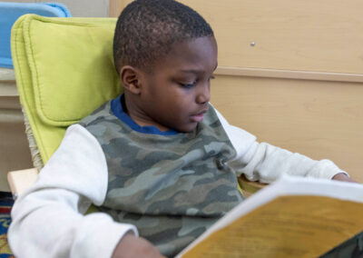 A boy in a small comfy chair looking at a picture book.