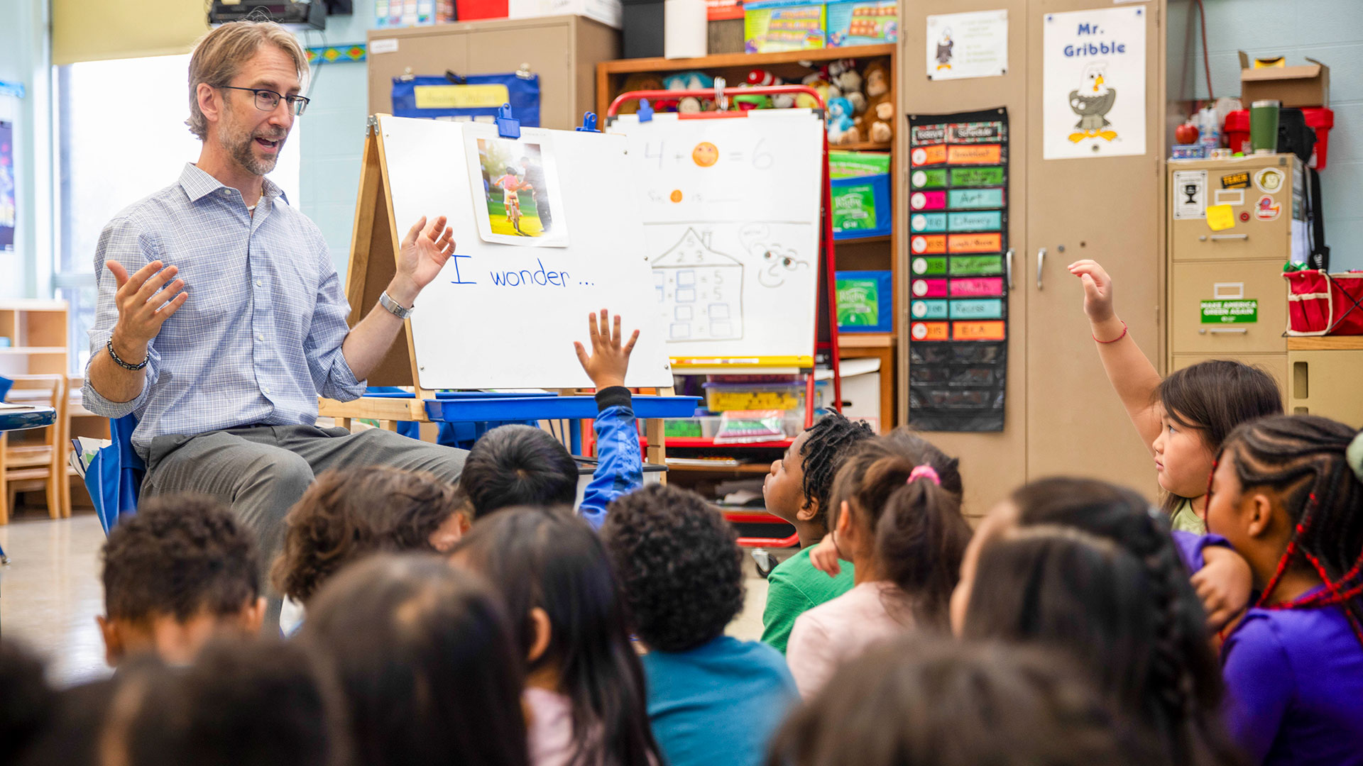 Young students sit at the feet of their teacher listening to him talk.