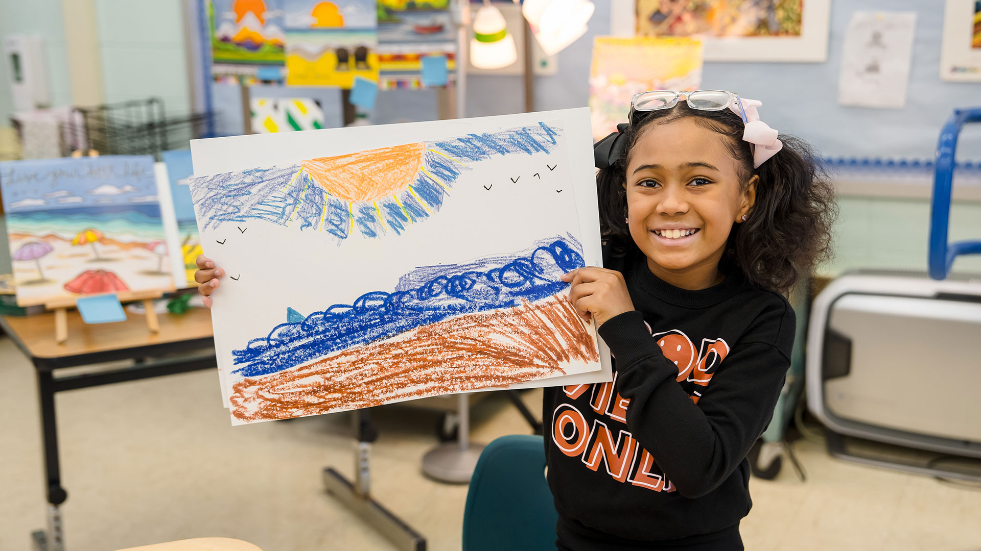 A child in a classroom holding up a drawing.
