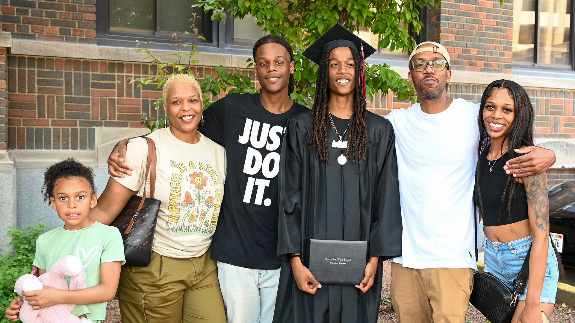 A graduate in a cap and gown smile with their family.