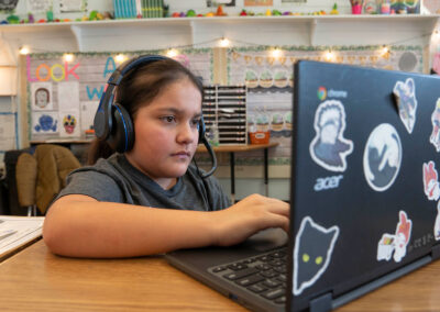 A child with headphones on uses a laptop with stickers on it.