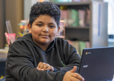 A boy looks at the camera while using a computer.