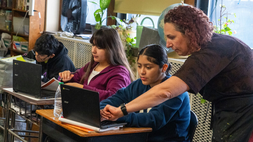 A teacher helps her students as they use computers.