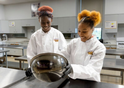 Two culinary students smile as they prepare food in a bowl.