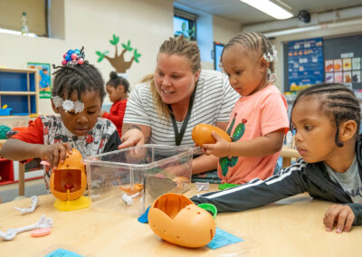 A teacher watches as her young students put a Mr. Potato Head together.