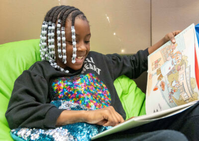 A young girl sits in a beanbag chair and looks at a picture book.