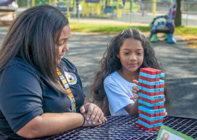 A teacher and student sit outside at a table and play a game with blocks that have equations on them.