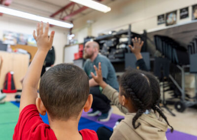 View from behind young children raising their hands with a teacher in front of them.