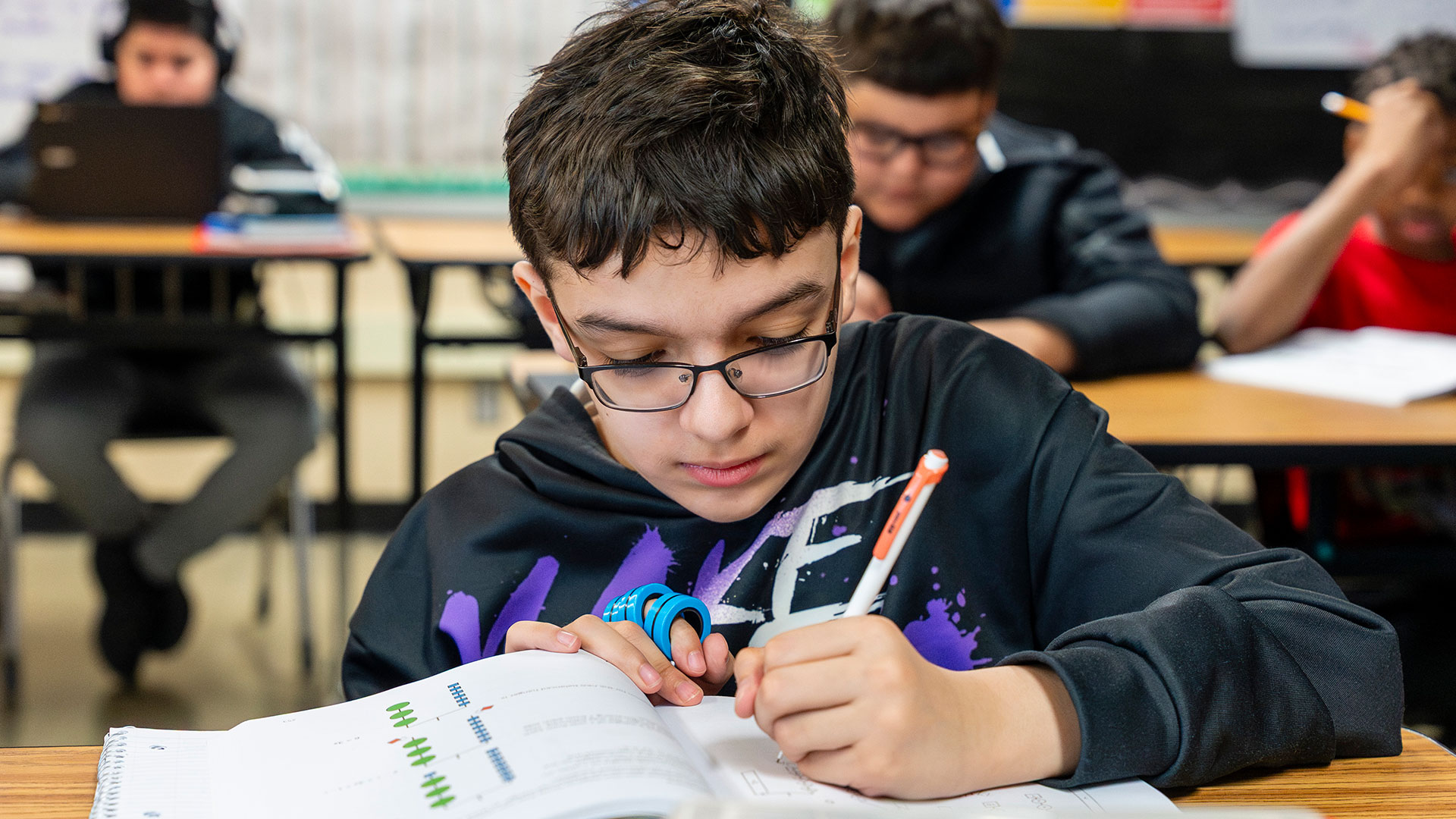 A student in a classroom writing in a workbook.