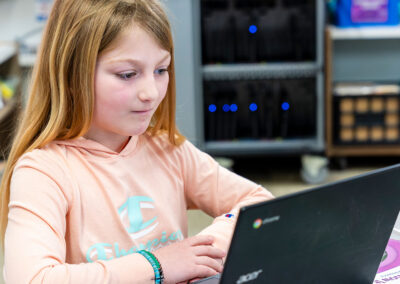 A girl in a class room looking at a laptop.