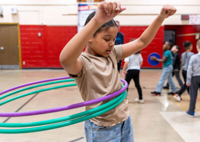 A girl in a gymnasium hula hooping.