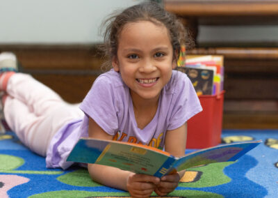 A girl laying on the floor reading a book.