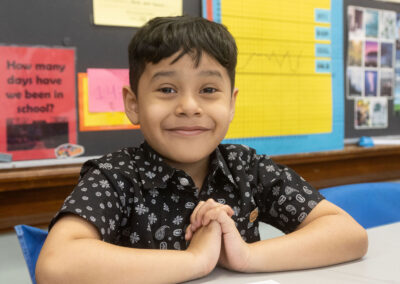 A boy in a classroom with his hands folded.