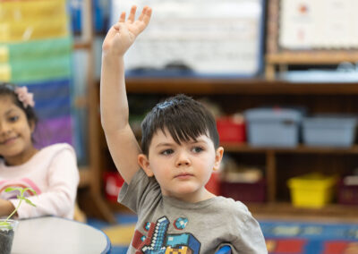 A classroom with young students raising their hands.